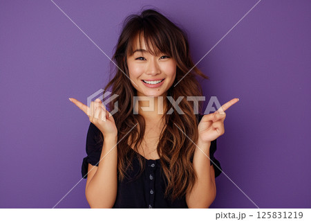 happy young woman pointing up, isolated on a purple background, in side view. Mockup for text and design. Asian girl wearing a white t-shirt, smiling and posing in a studio. 125831219