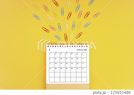 February 2026 desk calendar and paper clips on yellow background. 125831480