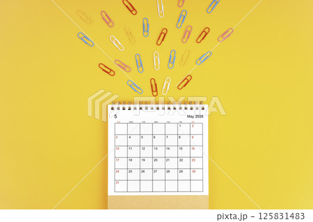 May 2026 desk calendar and paper clips on yellow background. 125831483