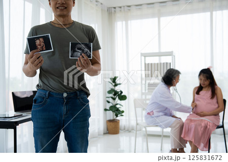 Asian husband hold ultrasound Images of His Unborn Child and pregnant women visit obstetrician for consulting in medical clinics or hospitals planning pregnancy. planning pregnancy, trust and respect 125831672