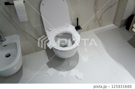A messy toilet scene with hygiene paper scattered on a white bathroom floor 125831688