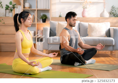 Young asian couple practicing yoga and meditation together in the living room at home. 125832173