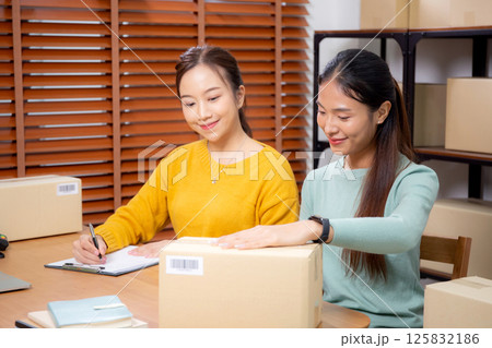 Two young asian woman working while planning online business and checking order with writing. Two young asian woman working while planning online business and checking order with writing. 125832186