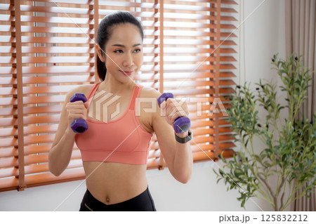 Young asian woman in sportswear workout with dumbbells for strength and strong in living room. Young asian woman in sportswear workout with dumbbells for strength and strong in living room. 125832212