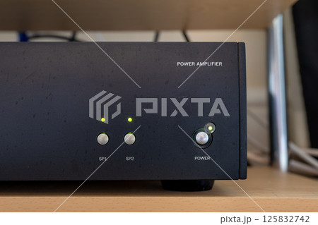 Black audio power amplifier without branding. Old, worn and dirty amplifier in hi-fi system. Switched on with LED lights glowing. Sitting on shelf with cables behind. Black audio power amplifier without branding. Old, worn and dirty amplifier in hi-fi system. Switched on with LED lights glowing. Sitting on shelf with cables behind. 125832742