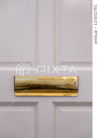 Gold-colored letter box on a white door. Old and worn. Gold-colored letter box on a white door. Old and worn. 125832761