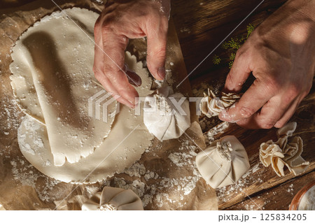 Hands expertly mold khinkali, the traditional Georgian dumplings, in bright sunlight, showcasing fresh ingredients and the art of cooking in action. 125834205