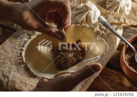 Hands expertly mold khinkali, the traditional Georgian dumplings, in bright sunlight, showcasing fresh ingredients and the art of cooking in action. 125834208