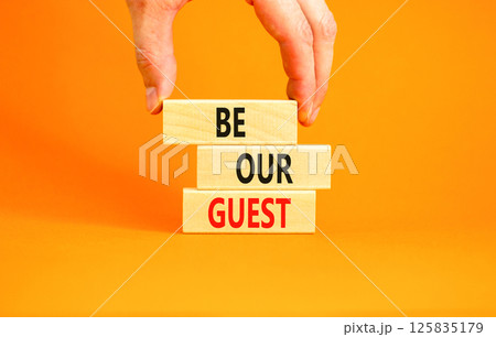 Be our guest symbol. Concept words Be our guest on beautiful wooden block. Businessman's hand. Beautiful orange background. Business and be our guest concept. Copy space. Be our guest symbol. Concept words Be our guest on beautiful wooden block. Businessman's hand. Beautiful orange background. Business and be our guest concept. Copy space. 125835179
