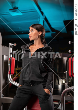 model poses confidently in sleek black activewear against backdrop of modern gym. lighting adds energetic vibe perfect for workout inspiration. 125836335