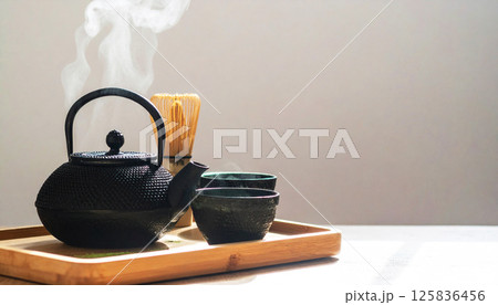 Japanese tea set with matcha powder and steam rising from a teapot on a wooden tray. Minimalist zen composition perfect for wellness, tea ceremony, or Japanese culture themes 125836456