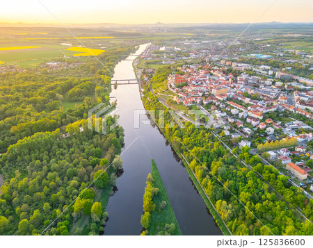 An aerial view captures the confluence of the Vltava and Labe rivers near Melnik, Czechia. The landscape features lush greenery, flowing waters, and a nearby town nestled against the rivers. 125836600
