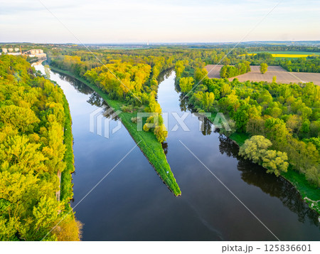Aerial view capturing the stunning confluence of the Vltava and Labe rivers near Melnik, Czechia. Lush greenery surrounds the rivers, showcasing natural beauty during a clear day. 125836601