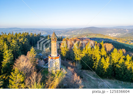 In a serene spring morning, the Stepanka Lookout Tower stands tall amidst lush green trees in Korenov, offering expansive views of the Jizera Mountains and surrounding landscape. In a serene spring morning, the Stepanka Lookout Tower stands tall amidst lush green trees in Korenov, offering expansive views of the Jizera Mountains and surrounding landscape. 125836604