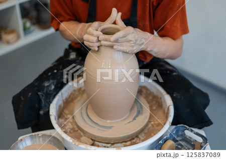 Close-up of a potter's hands making a ceramic vase on a potter's wheel.  125837089