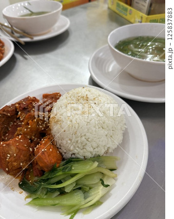 white Rice meat vegetables Close up Gourmet Meat Slices with Fresh Vegetables Above Rice, Placed on White Plate on Wooden Table. 125837883