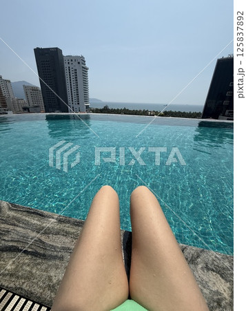 unrecognizable girl knees Poolside city view Woman relaxing by luxury hotel pool with city skyline. Leisure and travel. unrecognizable girl knees Poolside city view Woman relaxing by luxury hotel pool with city skyline. Leisure and travel. 125837892