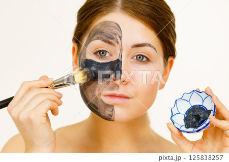 Female applying black mud mask to face 125838257