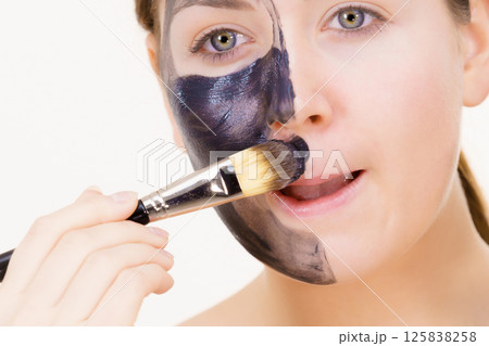 Female applying black mud facial mask Female applying black mud facial mask 125838258
