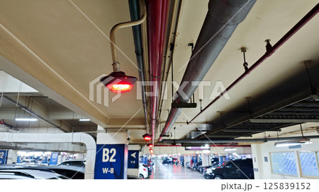 Red Parking Spot Indicator Light in Basement Car Parking Area with Exposed Pipes and Ceiling Fixtures 125839152