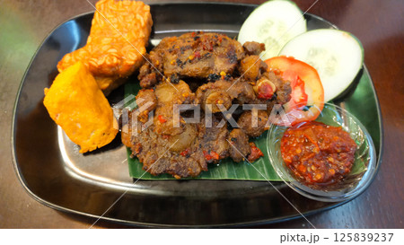 Spicy Grilled Oxtail with Tofu and Tempeh Served with Fresh Cucumber and Tomato Slices and Spicy Chili Sauce on Black Plate Spicy Grilled Oxtail with Tofu and Tempeh Served with Fresh Cucumber and Tomato Slices and Spicy Chili Sauce on Black Plate 125839237