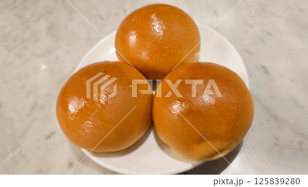 Three Golden Brown Barbecued Pork Buns on a White Plate with a Marble Background in a Restaurant Setting 125839280