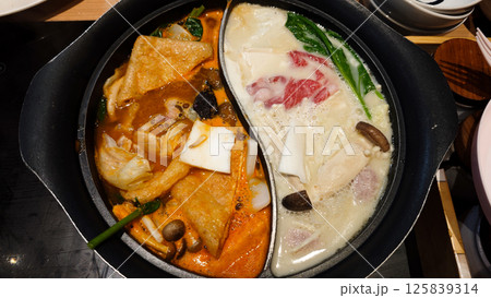 Dual Flavor Hot Pot with Spicy and Regular Broth Featuring Fresh Vegetables and Meats in a Restaurant Setting 125839314