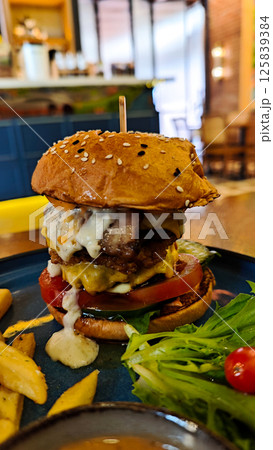A perfect Gourmet Cheeseburger with Beef Egg and Fries on Blue Plate in Cozy Cafe Setting with Bright Lighting and Wooden Table A perfect Gourmet Cheeseburger with Beef Egg and Fries on Blue Plate in Cozy Cafe Setting with Bright Lighting and Wooden Table 125839384