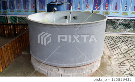 Large Circular Concrete Fish Tank with Water Filter System in an Outdoor Koi Farm Displaying Different Koi Fish Varieties on Illustrated Posters 125839433