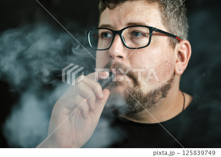 Young Caucasian man smoking an electronic cigarette portrait on black. 125839749