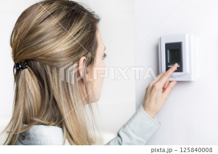 woman set the thermostat at house. woman set the thermostat at house. 125840008