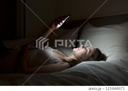 Woman using smartphone on bed at night Woman using smartphone on bed at night 125840071
