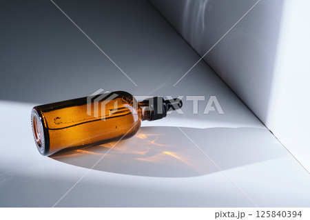 A bottle of serum made of brown glass on a white background with stripe of light. A bottle of serum made of brown glass on a white background with stripe of light. 125840394