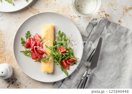 Delicious french omelette with cheese served with fresh vegetables and ham. Healthy diet food concept. Top view 125840448