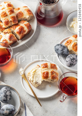Traditional Easter hot cross buns on white plate with butter, cup of tea and eggs. Delicious Easter breakfast 125840458