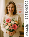 Smiling Woman Holding Flowers with Mother's Day Message in the Background 125840502