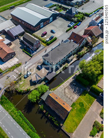 Aerial view of a Dutch village with houses, canals, roads, and industrial buildings. The peaceful scene shows a blend of residential and commercial architecture surrounded by greenery. 125840565