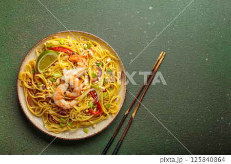 Pad thai noodles with shrimp, peanuts and lime on green background, dish of Thailand. Space for text 125840864