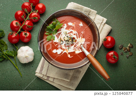Tomato soup with cream, pumpkin seeds and herbs on green background top view Tomato soup with cream, pumpkin seeds and herbs on green background top view 125840877