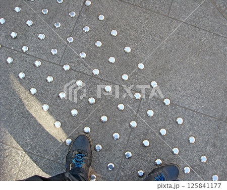 Old metal rivets on gray asphalt. Legs of traveler on an asphalt road 125841177