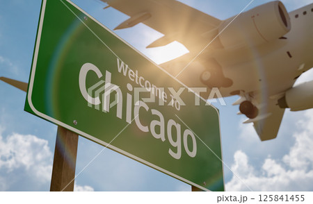 Welcome To Chicago Green Road Sign Against a Blue Sky and Clouds with Low Flying Airplane Above. Welcome To Chicago Green Road Sign Against a Blue Sky and Clouds with Low Flying Airplane Above. 125841455