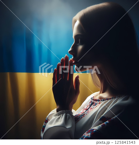 Woman praying in front of Ukrainian flag, traditional clothes, side profile 125841543
