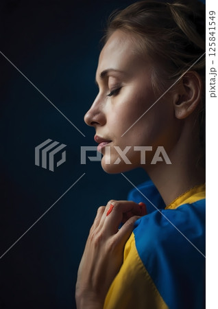 Woman praying in front of Ukrainian flag, traditional clothes, side profile 125841549