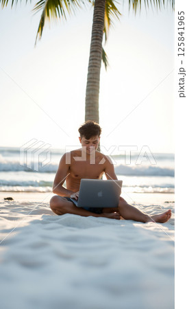 Freelancer guy works remotely on his laptop while sitting on the sand on a tropical beach 125841965