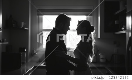 Married couple hugging in the morning in the kitchen. Man and woman in love hugging in the rays of the morning sun. Monochrome image.  125842152
