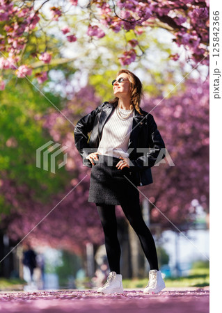Portrait scenic young adult pretty happy woman enjoy walking spring city street blooming pink cherry trees alley background in Magdeburg city. Female person joyful carefree  smiling outdoors 125842366