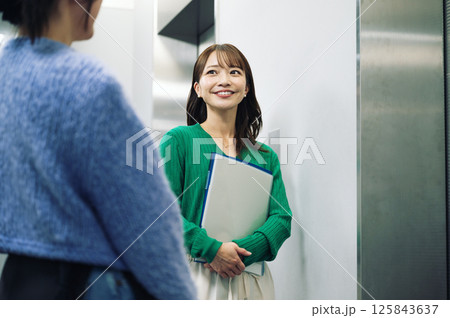 エレベーターの待ち時間に談笑をするキャリアウーマン エレベーターの待ち時間に談笑をするキャリアウーマン 125843637