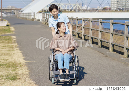 中年の女性が乗った車椅子を押して散歩する介護士 中年の女性が乗った車椅子を押して散歩する介護士 125843991
