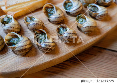 Escargot with garlic butter on wooden platter 125845729