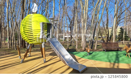 Modern playground with unique slide and spring riders in leafy park Modern playground with unique slide and spring riders in leafy park 125845800